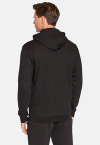 Schwarzer Kapuzenpullover mit weicher Textur, langen Ärmeln und gerippten Bündchen. Ausgestattet mit einer großen Kapuze auf der Rückseite und einem lockeren Sitz.