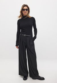 Black ribbed turtleneck top paired with high-waisted black pleated trousers. Accessories include a black belt and dark sunglasses.