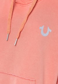 Felpa corallo realizzata in materiale morbido, con tasca a marsupio, cordini e un accento logo grigio chiaro sul petto.