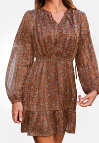 Abito floreale marrone realizzato in tessuto leggero, caratterizzato da lunghe maniche a sbuffo, una vita arricciata e un orlo ondulato. Design con scollo a V.