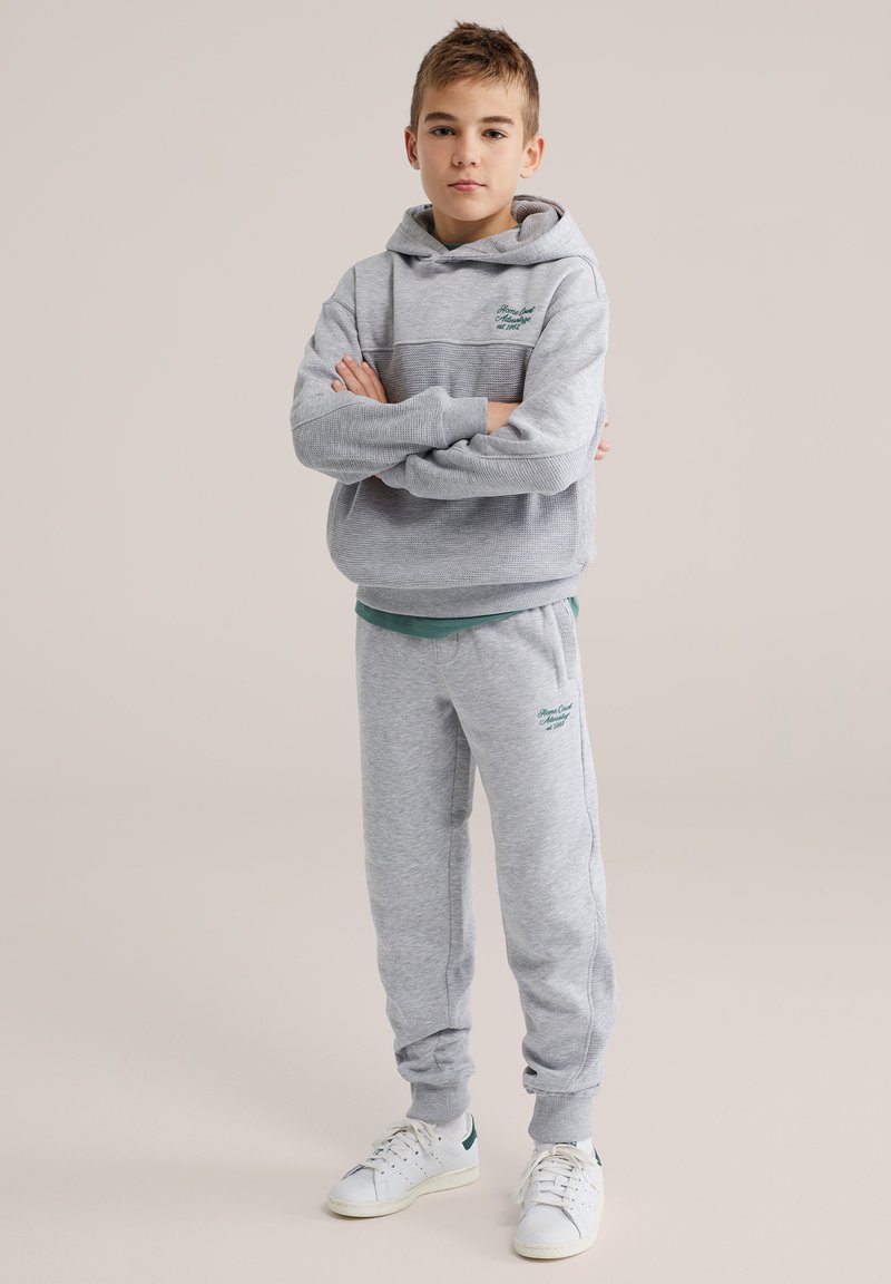 Szara bluza z kapturem o dwukolorowym wzorze, z kieszenią kangurką, w komplecie z dopasowanymi szarymi dresami. Oba elementy mają miękką teksturę i zielone akcenty.