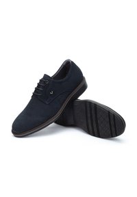 Mornarske sukenske cipele od suede materijala s dizajnom na vezivanje. Imaju izdržljiv crni gumeni potplat s teksturiranim uzorkom za bolje prianjanje.