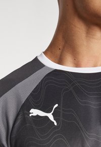 Fekete sport póló, textúrált dizájnnal, szürke részletekkel és fehér Puma logóval a mellrészen. Kerek fehér gallér.