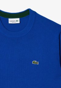 Maglione in cotone blu con colletto verde a coste, vestibilità regolare. Presenta un piccolo logo di coccodrillo ricamato in verde sul petto sinistro.