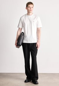 Biele bavlnené tričko s krátkym rukávom a malým logom, v kombinácii s čiernymi nohavicami a štruktúrovanou čiernou koženou taškou. Ploché topánky.