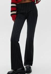Svarta, randiga utsvängda byxor gjorda av slätt tyg, med en figursydd midja. Kombineras med skinande svarta loafers med kedjedetalj.