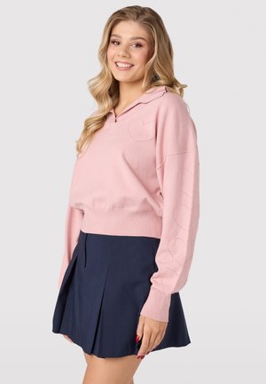 Light pink knitted pullover with a collar, featuring a heart pattern on the left chest and down the sleeves, paired with a dark navy pleated skirt.