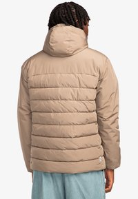 Beige puffer jacket with horizontal quilted design, a hood, and long sleeves. Smooth texture, standard fit, and a small brand tag at the hem.