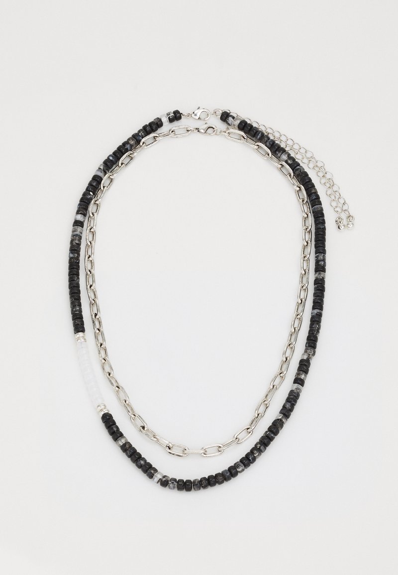 Collier multi-brins composé de perles noires et grises, entrecoupées de maillons de chaîne en argent et d'une perle d'accent transparente. Fermeture ajustable.