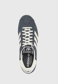 Adidas-sneakers i mörkblå denim med tre krämfärgade ränder, vita snörning och en logotyp på tungan. Texturerad innersula.