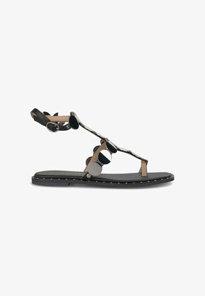 Sandalia plana con base negra, correas de cuero marrón, acentos metálicos circulares y detalle de bordes con tachuelas. Diseño con punta abierta y correa para el tobillo.