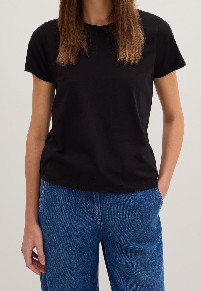 T-shirt noir à manches courtes en coton doux, doté d'un col rond classique et d'une coupe décontractée. Associé à un pantalon en denim bleu.