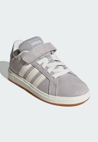 Baskets en daim gris avec des rayures en cuir blanc, bout arrondi, devant à lacets, et sangle velcro réglable. Semelle en caoutchouc blanc avec texture antidérapante.