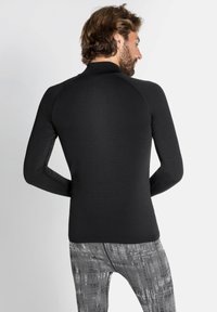 Zwart sportshirt met lange mouwen van textuurstof en een getailleerd ontwerp, met een hoge kraag en raglanmouwen.