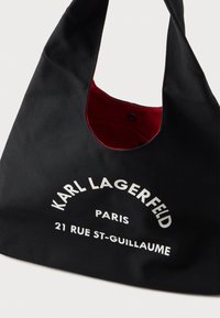 Fekete szövet bevásárlótáska piros belső béléssel, elől fehér "KARL LAGERFELD PARIS 21 RUE ST-GUILLAUME" felirattal és mágneses záródással belül.