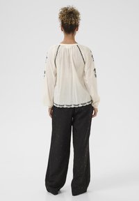 Hvid bluse med sort broderi, lange ærmer og samlet ryg. Sammen med løse sorte bukser med et diskret stjernemønster.