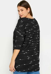 Svart tröja med vita horisontella ränder, med trekvartslånga ärmar och knappar som detalj på ärmarna. Ribbad textur på tyget.