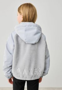 Ljust grå hoodie-jacka med en mjuk fleece-bakdel, som har ordet "BAKER" präglat på nedre delen av ryggen. Mjuk textur och sportig design.