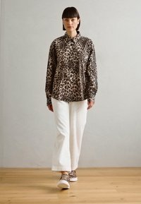 Lepard trykk knapp skjorte, lange ermer, kombinert med hvite vidde bukser og mønstrede slip-on sko. Glatt stoff, avslappet passform.