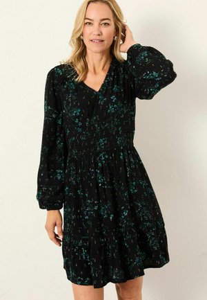 Black dress with a V-neck and long sleeves, featuring a smocked waist, tiered skirt, and green floral print throughout.