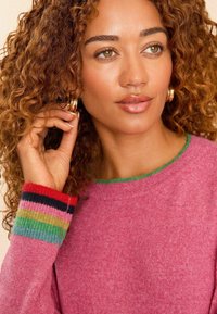 Ružový sveter s rebrovanými manžetami a viacfarebnými pruhmi. Mäkká textúra, okrúhly výstrih a smaragdovo zelený akcent na golieri.