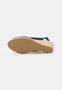 Sandale compensée marine avec un talon en jute tressé, semelle en caoutchouc texturé avec un motif en zigzag et une sangle à boucle réglable.