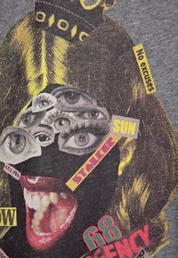 Camiseta gráfica que presenta un atrevido collage de ojos y una boca sobre una tela gris. Los acentos incluyen texto en amarillo y rosa con varias frases.