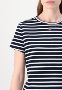Camiseta de rayas azul marino y blanca de manga corta, con textura acanalada y un pequeño logotipo en el pecho. Cuello redondo clásico.