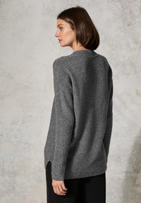 Pull gris côtelé avec un col rond, fentes sur les côtés et un tissu texturé. Le design présente des manches longues et une coupe décontractée.