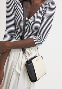 Borsa a tracolla in bianco e nero con una forma strutturata, caratterizzata da una texture liscia, un accento a catena e una tasca con pattina anteriore.