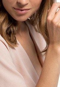 Nahaufnahme der Schulter und Hand einer Person, die ein weiches, blassrosa Oberteil mit glatter Textur und lässigem Schnitt trägt. Der Hautton ist gleichmäßig.