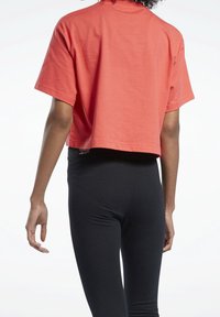 Korálové zkrácené tričko, krátké rukávy, měkký bavlněný materiál. V kombinaci s černými legínami s vysokým pasem, hladká textura, elastický střih.