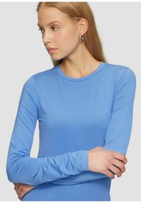 Langärmliges, hellblaues Oberteil aus weichem Stoff, mit rundem Ausschnitt und figurbetontem Schnitt. Minimalistische Ästhetik mit glatter Textur.