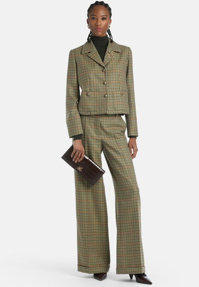 Groen en bruin geruit pak met een cropped, dubbelzijdige jas en brede broekspijpen. Gecombineerd met een donkere clutch en een zwarte coltrui.