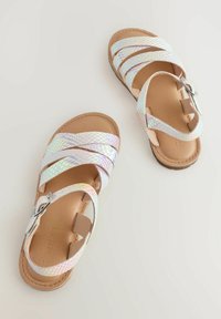 Le sandali con cinturini iridescenti presentano dettagli intrecciati, una fibbia argento e una suola beige, con un design a bande incrociate per una maggiore traspirabilità.