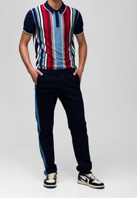 Pikétröja med vertikala röda, blå och vita ränder, marinblå krage och kant; kombinerad med marinblå byxor med blå sidoremsa; svarta och blå sneakers.