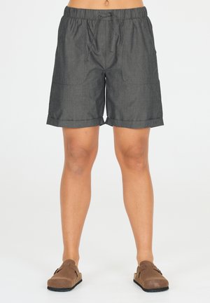 Shorts gris, arrivant au genou, avec une taille élastique et un cordon de serrage. Comprend deux poches avant et des poignets retroussés. Portés avec des chaussures brunes à enfiler.