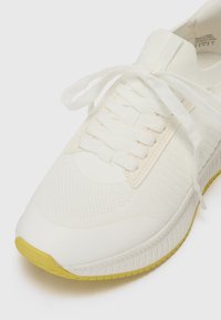 Baskets blanches avec tige texturée, lacets blancs plats et semelle extérieure en caoutchouc jaune. Présente une pointe lisse et des accents nervurés.