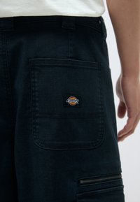 Μαύρο τζιν παντελόνι με ορθογώνια πίσω τσέπη με λογότυπο και τσέπη με φερμουάρ στο πλάι. Δομημένο, ανθεκτικό υλικό με ορατές ραφές.