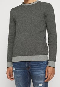 Grauer strukturierten Rundhalsausschnitt-Pullover mit einem schwachen Muster, gerippten Bündchen und Saum, kombiniert mit ausgewaschenen blauen Jeans.