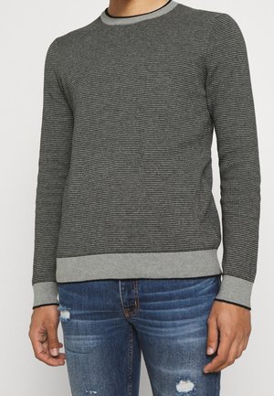 Pull en maille gris texturé avec un motif léger, poignets et ourlet côtelés, associé à un jean bleu déchiré.