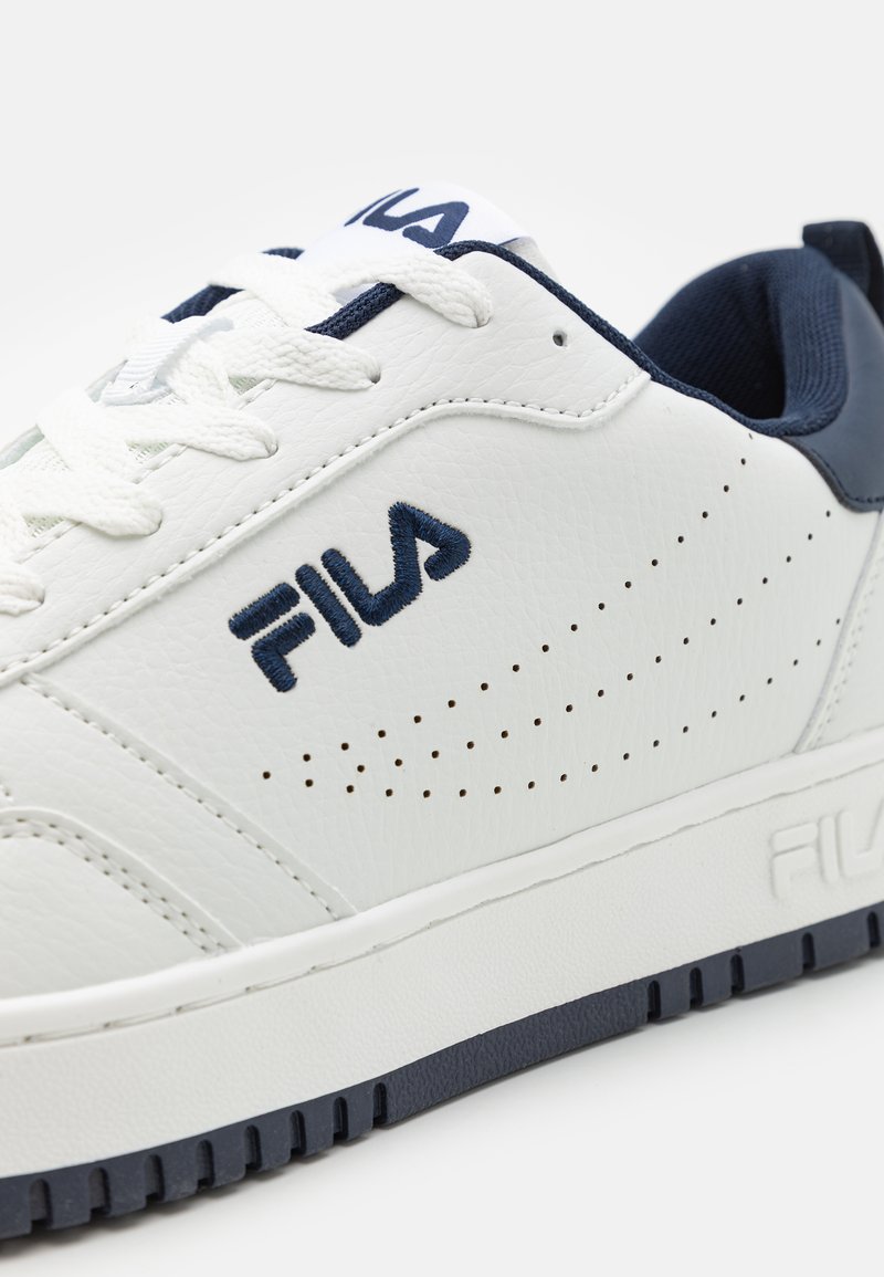 Baskets en cuir blanc avec accents bleu marine, texture perforée, logo brodé bien visible et semelle texturée. Lacets et col rembourré inclus.