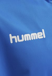 Blauw sportshirt van textuurstof met het witte logo "hummel" prominent weergegeven.
