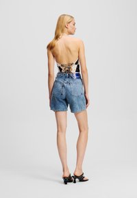 Denim kratke hlače z ohlapnim krojem, svetlo modre barve in raztrganimi robovi, v kombinaciji z bodijem z vezanjem na hrbtu, ki ima vzorčasto zasnovo.