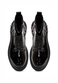 Mustat nahkaiset nilkkasaappaat, joissa on kiiltävä pinta, nauhakiinnitys, teksturoidut sivut ja metallikoristeet. Littee kumipohja.