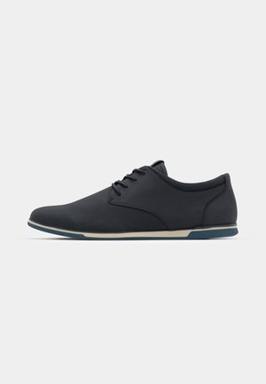 Schwarze Schnürschuhe mit einer glatten, strukturierten Oberseite, einer abgerundeten Spitze und einer kontrastierenden beigen Sohle. Minimalistisches Design mit dezenten Akzenten.