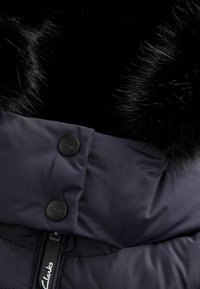 Giacca puffer blu navy con colletto in finta pelliccia nera, dotata di due bottoni neri circolari e una zip, texture liscia e design trapuntato.