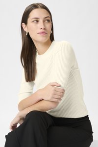 Ribbet striktrøje i off-white med rund halsudskæring og ærmer til albuerne, sat sammen med sorte bukser. Glat tekstur, tætsiddende design.