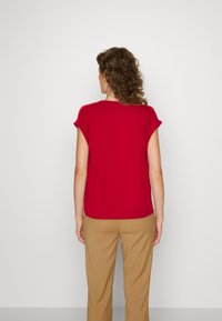 Haut rouge à manches courtes, coupe décontractée, col rond et texture lisse. Associé à un pantalon beige à jambes larges en tissu doux.