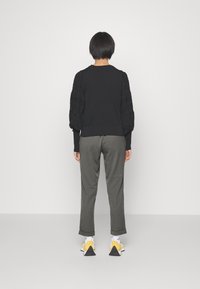 Svart tröja med texturerade puffärmar, kombinerad med olivgröna byxor. Vita strumpor och sneakers med gula detaljer fulländar outfiten.